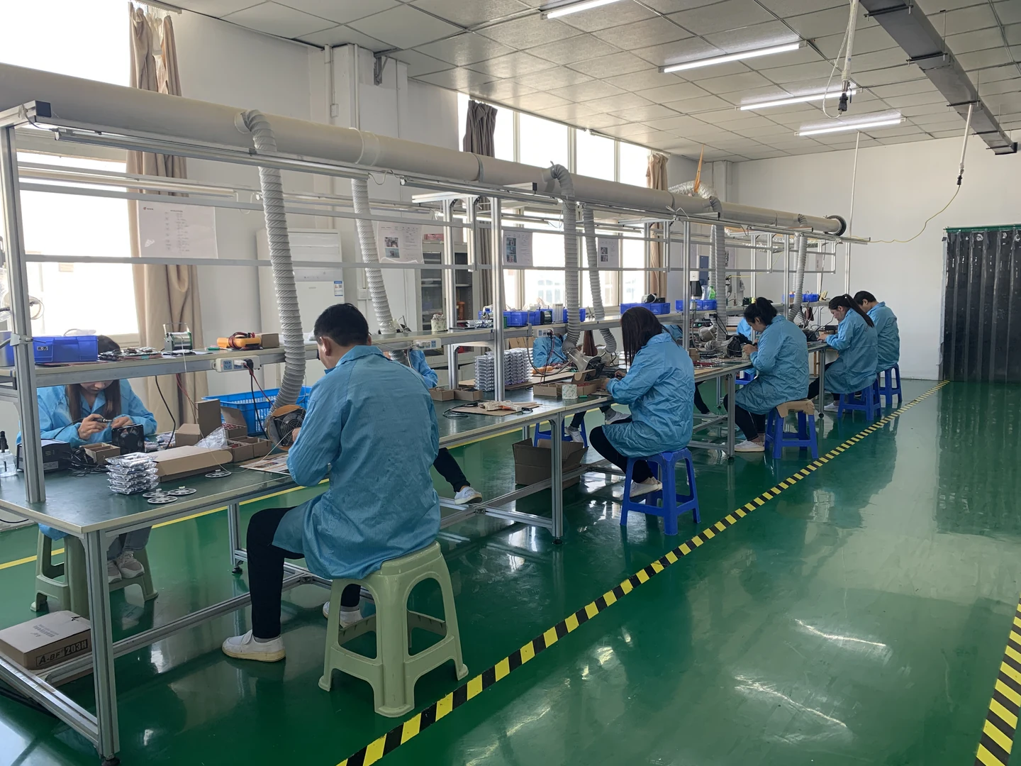 Workers assembling components at a row of workbenches in a supplied NOKIN factory photograph